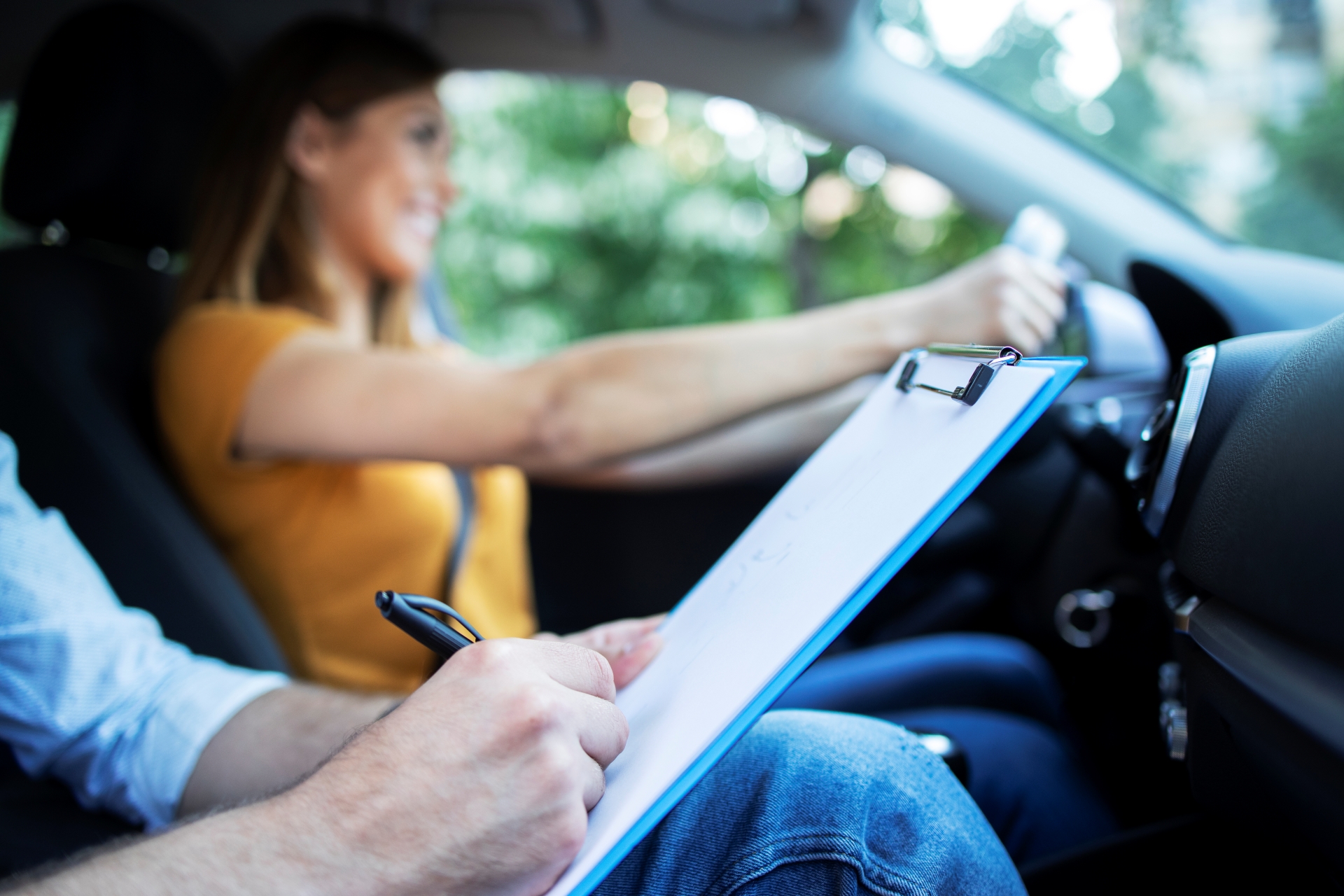 ¡Conducir desde los 17! Así será el nuevo carnet de conducir europeo vista de cerca del instructor de conduccion sosteniendo la lista de verificacion mientras que en el fondo la estudiante conduce y conduce el automovil - ¡Conducir desde los 17! Así será el nuevo carnet de conducir europeo